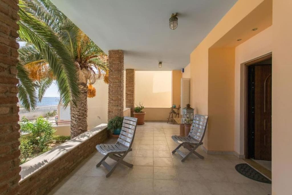 Shaded porch with palm tree at a beachfront apartment in Artemida, Greece